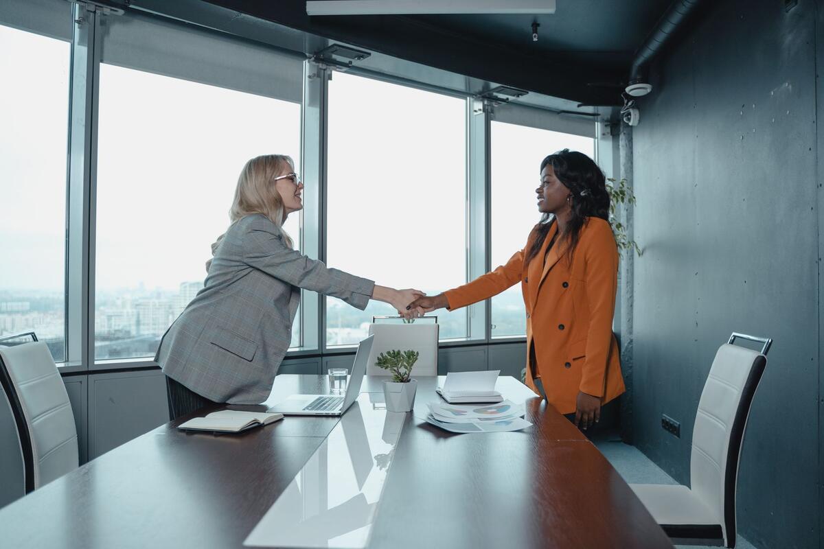 Two professionals shaking hands across a conference table in a high-rise office