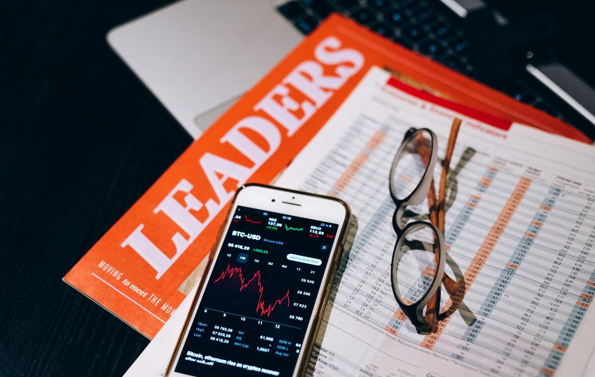 Financial reports, reading glasses, and a smartphone showing a market price chart on a desk